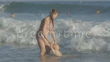 年轻的白种人母亲和两岁的金发碧眼的婴儿在海边玩水浪溅的游戏